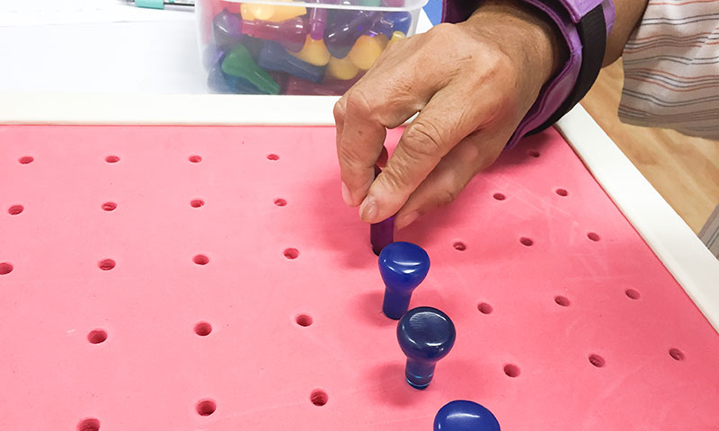 Person placing pegs on a board during rehab