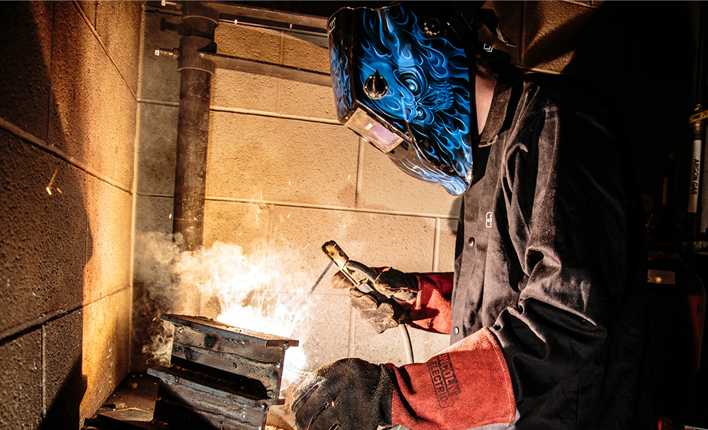 Graphic of Cleveland State student in the welding department with mask on welding metal with sparks flying.